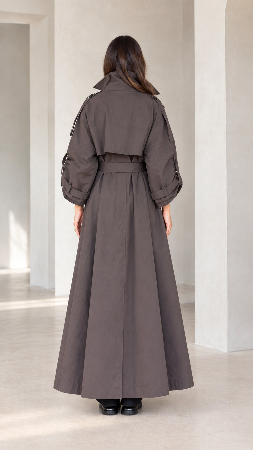 Back view of woman wearing charcoal brown belted maxi trench coat showing storm flap