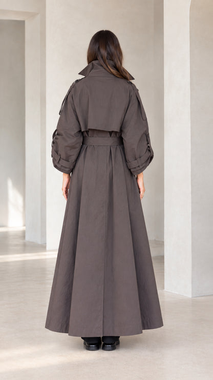 Back view of woman wearing charcoal brown belted maxi trench coat showing storm flap