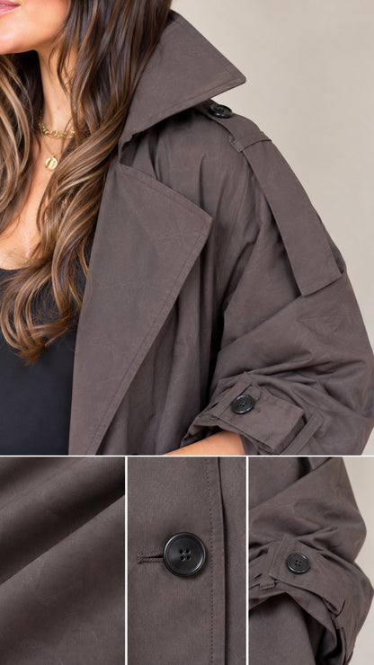 Close-up detail of charcoal brown maxi trench coat showing lapel, buttons, and sleeve cuff